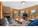Cozy living room with a stone fireplace, wood-paneled walls, and large windows offering serene outdoor views at 27231 Log Trl, Conifer, CO 80433