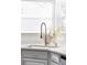 A close-up of a kitchen sink features a modern faucet, white countertops, neutral cabinets and bright natural light at 674 Huntington Dr, Highlands Ranch, CO 80126