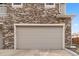 Attached two-car garage with neutral door, stone accents, and exterior lighting at 24747 E Calhoun Pl # C, Aurora, CO 80016