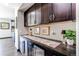 Stylish bar area with dark wood cabinets, decorative accents, and a view into the kitchen at 25338 E Costilla Pl, Aurora, CO 80016