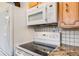 Kitchen featuring white appliances, electric cooktop, microwave, and cabinets with tiled backsplash at 2837 Reed St, Wheat Ridge, CO 80033