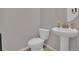 This powder room features a toilet, pedestal sink, round mirror, and neutral-colored walls and tile at 16048 Elizabeth St, Thornton, CO 80602