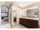 Spacious bathroom with double vanity sinks, large mirror, and an arched doorway leading to the bedroom at 15907 W 72Nd Dr, Arvada, CO 80007
