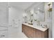 A well-lit bathroom featuring double sinks, a marble tiled shower, modern lighting fixtures and updated cabinets at 3798 S Wabash St, Denver, CO 80237