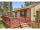 Exterior view of a tan home featuring a wooden deck and mature trees, nestled among lush greenery at 30400 Hilltop Dr, Evergreen, CO 80439