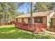 Charming single-story home featuring a red deck, green lawn, and mature trees at 30400 Hilltop Dr, Evergreen, CO 80439