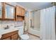 Classic bathroom with wood cabinets, floral wallpaper, and a shower over tub with white tiling at 366 Kenton St, Aurora, CO 80010