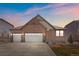 Charming exterior elevation showcases a stone facade, two-car garage, and well-manicured lawn against a colorful twilight sky at 27234 E Quarto Ave, Aurora, CO 80016