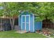 Backyard shed nestled beneath lush trees with a ramp, double doors, and adjacent trash receptacle at 4879 S Johnson St, Littleton, CO 80123
