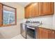 Bright laundry room with window, wood cabinets, and stainless steel washer and dryer at 13314 Spruce Creek Cir, Larkspur, CO 80118
