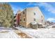 Tan building exterior with a walkway and snowy landscaping at 10872 W Evans Ave # 2E, Lakewood, CO 80227