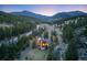 Panoramic aerial view of a mountain home nestled among dense trees with a scenic mountain backdrop at dusk at 24 Pine Valley Rd, Evergreen, CO 80439