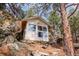 Cozy cabin nestled amongst trees and boulders, featuring large windows with natural light, and light colored siding at 24 Pine Valley Rd, Evergreen, CO 80439