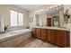 Bright bathroom with a large tub, dual sinks, wood-look tile floors, and neutral colors at 1051 Bramblewood Dr, Castle Pines, CO 80108