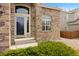 Inviting front entrance featuring a well-lit porch, manicured shrubs, and stone accents at 13078 Monaco Way, Thornton, CO 80602