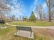 Green metal bench on a concrete slab overlooking a large green field with walkways and trees in Bonnie Brae Park at 755 S Milwaukee St, Denver, CO 80209