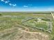 A sprawling aerial view of land showcasing a brown home and large shop, surrounded by green fields at 68251 E 96Th Ave, Byers, CO 80103