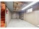 Unfinished basement space with exposed ceiling, red stairs, and built-in shelving, offering storage and utility at 392 Central Ave, Brighton, CO 80601