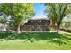 Expansive backyard featuring a lush lawn, mature trees, and a brick home exterior with an outdoor patio seating area at 10366 E Ida Ave, Greenwood Village, CO 80111