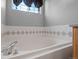 Close-up of bathroom soaking tub featuring bright window, tiled surround, and sleek chrome fixtures at 1479 Nemrick Pl, Castle Rock, CO 80109
