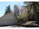 View of a white garage with an automatic door, complemented by landscaped bushes and tall pine trees at 28650 Cavan Ln, Evergreen, CO 80439