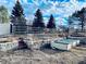 A backyard with raised garden beds, a wooden fence, and mature trees against a partly cloudy sky at 7194 S Himalaya Way, Centennial, CO 80016