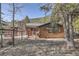 Cozy log cabin-style home with a stone chimney and fenced yard surrounded by trees at 10439 Christopher Dr, Conifer, CO 80433