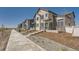 Modern townhome exteriors with light colored wood siding and brick accents along a sidewalk under a bright blue sky at 1224 S Algonquian St, Aurora, CO 80018