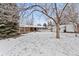 A snowy backyard features a covered patio, a fire pit, and a charming white picket fence at 977 S Reed St, Lakewood, CO 80226