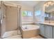 Bright bathroom features a tub next to a window, a glass shower, and light blue cabinets at 9921 W Edenburg Pl, Littleton, CO 80127