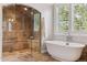 Bright bathroom with glass shower, soaking tub, large window with shutters, and stone tile flooring at 115 S Glencoe, Denver, CO 80246