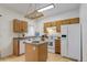 Bright kitchen featuring wood cabinets, an island, stainless sink, white appliances, and a hanging rack at 4504 S Cimmarron Cir # D, Aurora, CO 80015