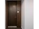 Hallway view of a dark wood-finished unit door with a silver handle and room number 