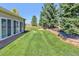 Large grassy backyard featuring manicured landscaping, privacy trees and a fire pit area at 18399 Wagon Trl, Mead, CO 80542