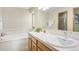 Bright bathroom featuring a soaking tub with tile surround, spacious vanity with tiled countertop and framed mirror at 18399 Wagon Trl, Mead, CO 80542