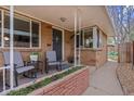Inviting front porch with brick planter, seating, and a blue striped welcome mat in front of the front door at 3667 Hudson St, Denver, CO 80207