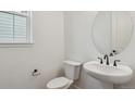 Modern half bathroom with a pedestal sink, round mirror, and black fixtures at 8230 Snake River St, Littleton, CO 80125