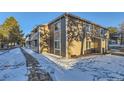 Exterior view of condo with stone facade and brown siding and a snowy yard at 18105 E Ohio Ave # 102, Aurora, CO 80017