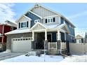 Two-story home with stone accents and a covered front porch, featuring a two-car garage, located in a snow-covered neighborhood at 1048 Larkspur Dr, Erie, CO 80516