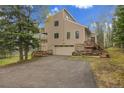 Two-story house with a two-car garage, balcony, stone accents, and a paved driveway, surrounded by a natural landscape at 2654 Sinton Rd, Evergreen, CO 80439