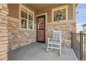 Inviting front porch features stone accents, a cozy rocking chair, and a decorative wreath on the window at 25059 E Alder Dr, Aurora, CO 80016