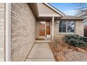 Inviting brick home entrance featuring a wooden door, brick exterior, and manicured landscaping at 2687 E 124Th Pl, Thornton, CO 80241