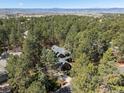 Aerial view of a home nestled among a dense forest of mature trees and distant mountain views at 484 Hyland Dr, Castle Rock, CO 80108