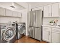 Well-lit laundry area with stainless steel washer, dryer, and refrigerator situated next to white kitchen cabinetry at 1827 Quail St # 8, Lakewood, CO 80215