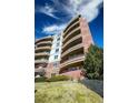 View of multi-story building with curved balconies and red brick facade, enhanced by green landscaping at 4875 S Monaco St # 103, Denver, CO 80237