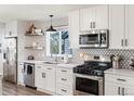 Modern kitchen with white cabinets, stainless steel appliances, geometric backsplash, and floating shelves at 17067 Motsenbocker Way, Parker, CO 80134