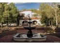 Estate featuring a tiered fountain, red roof, arched entrance, brick pathway, and mature landscaping at 3 Carriage Brook Rd, Cherry Hills Village, CO 80121