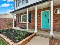 Inviting front porch with brick columns, a vibrant turquoise door, and manicured garden beds at 13935 E Idaho Pl, Aurora, CO 80012