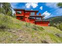 Hillside view of the modern red home, featuring large windows and sleek architectural design at 5896 Peregrine Trl, Golden, CO 80403