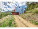 Modern home on a hillside with a metal facade and garage, accessible by a dirt driveway at 5896 Peregrine Trl, Golden, CO 80403